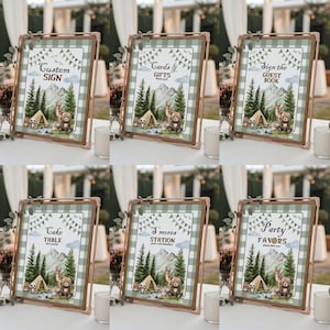 May include: A set of six framed signs with a camping theme. Each sign features a green and white checkered background, illustrations of a tent, trees, mountains, and animals, and text such as "Custom Sign" and "Cards & Gifts". The frames are a light brown color.