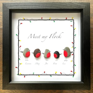 May include: Framed artwork with the text "Meet my Flock." The artwork features six pebble birds with red breasts, gray and brown bodies, and wire legs. The frame is black, and the artwork is decorated with a string of colorful lights.