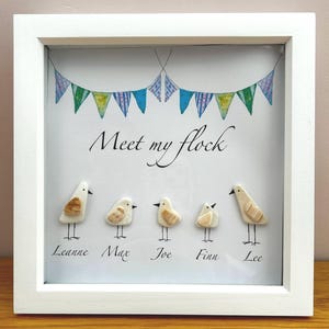 May include: A framed artwork featuring five small, handcrafted bird figures beneath a banner of colorful pennants. The phrase "Meet my flock" is written above the birds, with names below. The frame is white.
