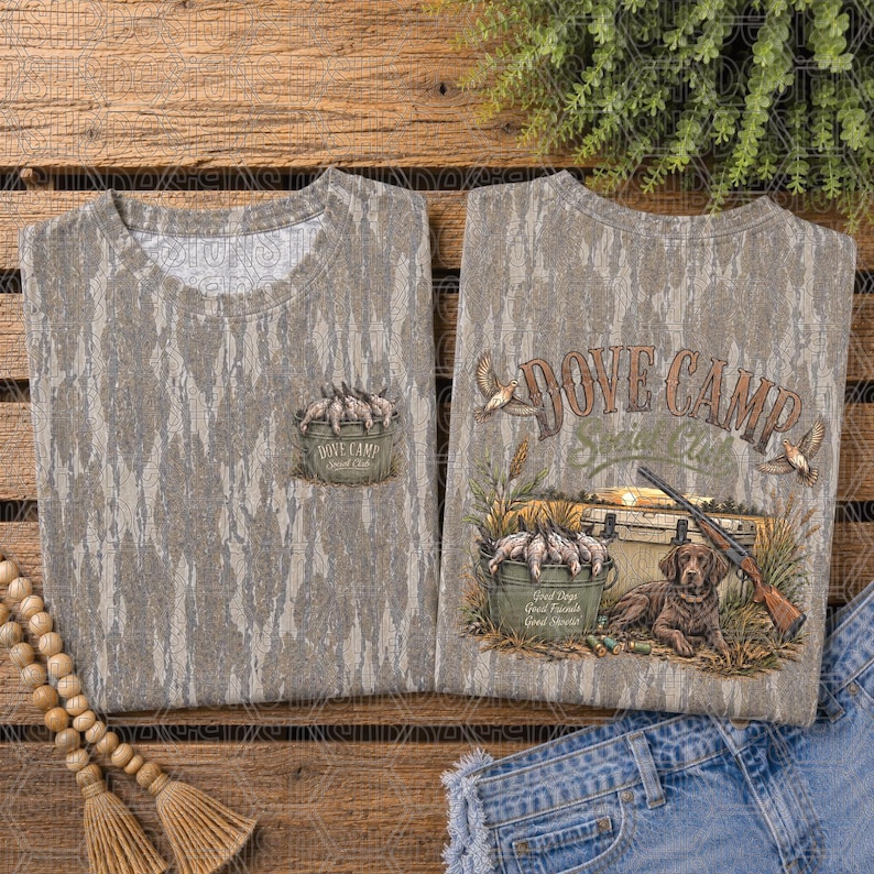 May include: A camouflage print t-shirt featuring a small graphic on the chest of a bucket filled with doves and the text Dove Camp. The back displays a larger graphic of a dog, a shotgun, a bucket of doves, and the text Dove Camp Social Club.
