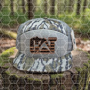Puede incluir: Gorra de b&eacute;isbol con estampado de camuflaje y visera plana. La parte delantera presenta un logotipo con las letras "CAT" en un dise&ntilde;o que se asemeja a la bandera estadounidense, con estrellas y rayas. La gorra es en tonos verdes, marrones y grises.