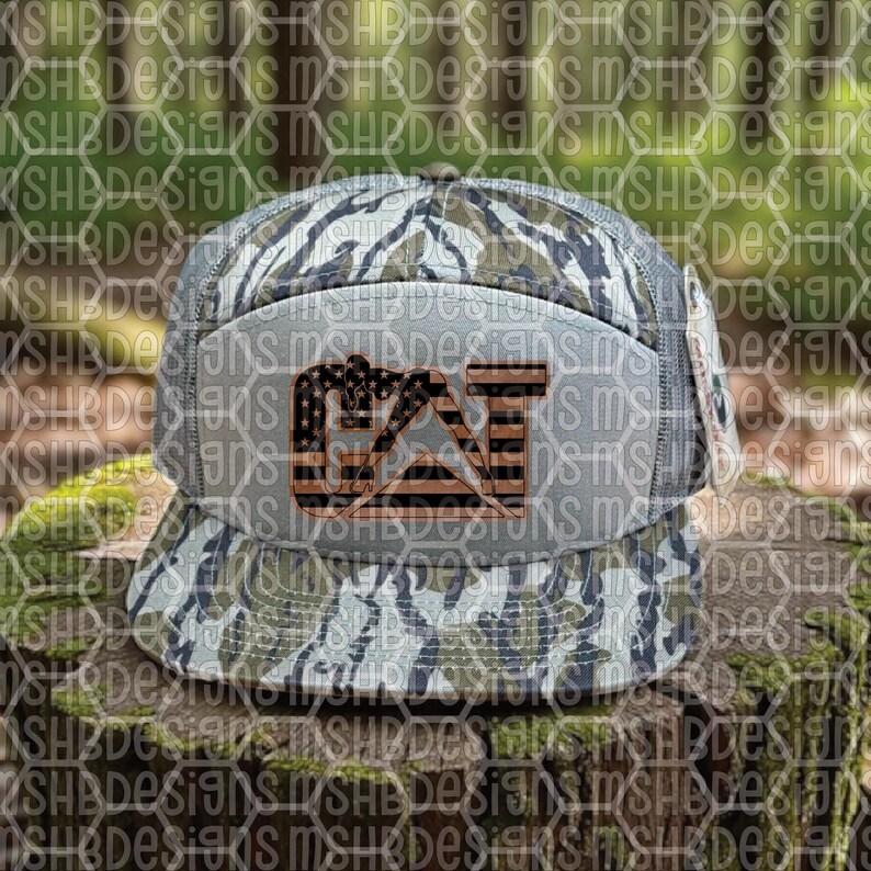 Puede incluir: Gorra de b&eacute;isbol con estampado de camuflaje y visera plana. La parte delantera presenta un logotipo con las letras "CAT" en un dise&ntilde;o que se asemeja a la bandera estadounidense, con estrellas y rayas. La gorra es en tonos verdes, marrones y grises.
