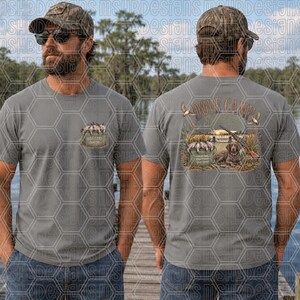May include: A grey t-shirt featuring a small graphic on the front left chest and a larger graphic on the back. The back design shows a hunting dog, a shotgun, and a bucket of ducks with the text Dove Camp, with a similar bucket design on the front.