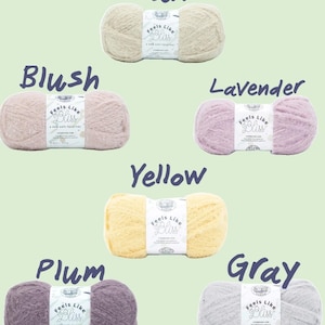 Op de afbeelding: Een verzameling garen in diverse kleuren: wit, zwart, bruin, roze, lavendel, geel, pruim, grijs, bruin en blauw. Elk garen heeft een label met "Feels Like Bliss".