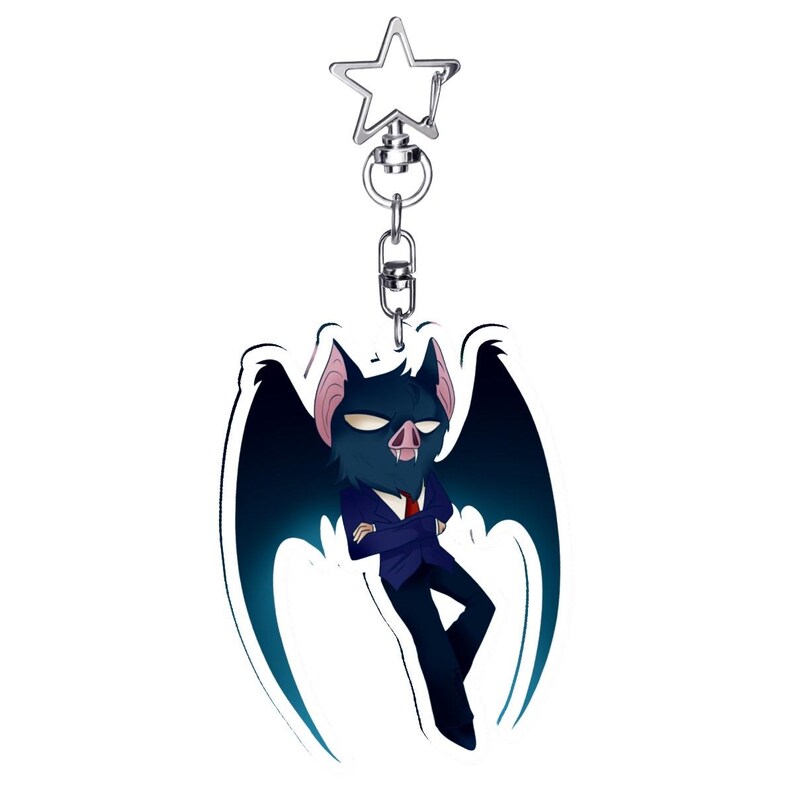 May include: A novelty keychain featuring a cartoon bat character in a blue suit and red tie. The bat has dark blue wings and a stern expression. The keychain has a silver-colored star-shaped clasp.