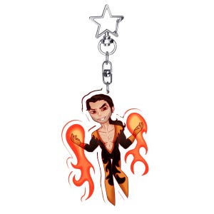 May include: A keychain featuring a cartoon character with a fiery theme. The character is depicted with orange and black attire, surrounded by stylized flames. The keychain has a silver star-shaped clasp.