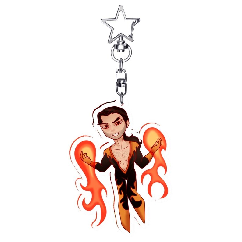 May include: A keychain featuring a cartoon character with a fiery theme. The character is depicted with orange and black attire, surrounded by stylized flames. The keychain has a silver star-shaped clasp.