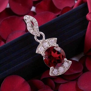 Peut inclure: Un pendentif argenté orné d'une grande pierre précieuse ronde rouge foncé au centre. Le pendentif est agrémenté de petites pierres claires et scintillantes disposées sur les bords supérieur et inférieur, avec une bélière décorative incrustée.