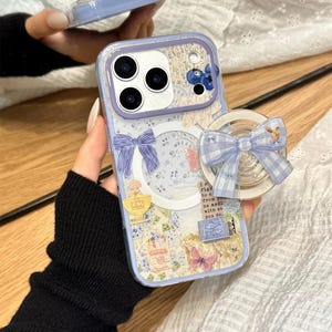 Könnte beinhalten: Eine transparente Handyhülle mit hellblauem Rand und floralem Design. Die Hülle hat eine Schleife, einen Schmetterling und einen Pop-up-Griff mit einem Hasen und einer blau-weiß karierten Schleife. Die Hülle hat eine transparente Rückseite mit floralem Design.