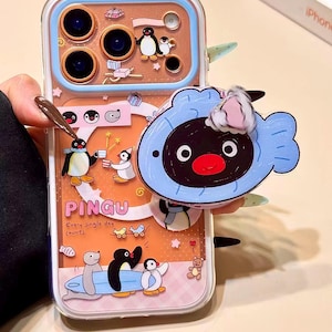 Puede incluir: Funda transparente para teléfono con un tema de dibujos animados de pingüinos, con la palabra "PINGU". La funda tiene una combinación de colores azul y rosa con varias ilustraciones de pingüinos y un personaje azul adjunto en la parte posterior.