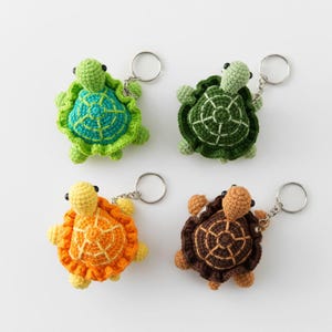 May include: Four crocheted turtle keychains in various colors: green with blue, dark green, orange, and brown. Each turtle has a silver keyring attached. The turtles are handmade and feature detailed shell patterns.