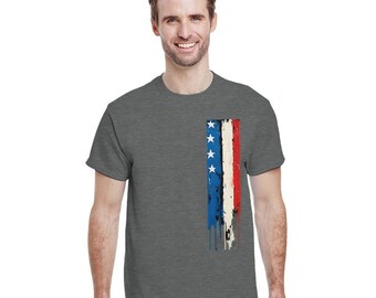 Può includere: Una maglietta grigio scuro con un disegno verticale della bandiera americana sul lato sinistro. Il disegno della bandiera include stelle bianche su una striscia blu, con strisce rosse e bianche sottostanti. Il design ha un aspetto vintage.