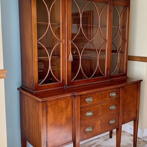 May include: A wooden hutch with glass-paned doors and three drawers. The cabinet is made of dark wood and features decorative brass hardware. The glass doors have an arched design. The hutch has a classic, traditional style.
