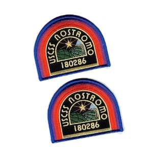 Peut inclure: Deux écussons brodés en forme de demi-cercle avec un fond noir, une étoile dorée, des collines vertes et le texte USCSS NOSTROMO 180286. Le motif est bordé par des bandes concentriques rouge, orange et bleue, avec un contour bleu brodé.