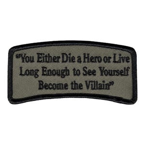 May include: A rectangular olive green embroidered patch with rounded corners and a black stitched border. The patch features the black embroidered text: "You Either Die a Hero or Live Long Enough to See Yourself Become the Villain" in a serif font.