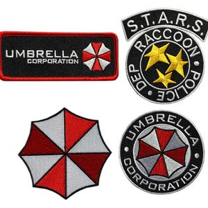 Puede incluir: Un conjunto de cuatro parches bordados que incluyen el logotipo de Umbrella Corporation en formas rectangulares y circulares, un parche circular del Raccoon Police Department S.T.A.R.S. con tres estrellas amarillas y un icono de paraguas rojo y blanco.
