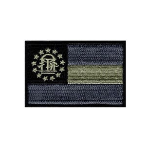 May include: A rectangular embroidered patch featuring a dark blue and olive green color scheme. The design includes a black canton on the left with a circular arrangement of thirteen embroidered stars surrounding a central arch and pillar emblem.