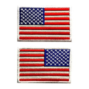 May include: Two rectangular embroidered patches featuring the United States flag design. Each patch displays a blue canton with white star-like stitching and alternating horizontal red and white stripes, finished with a stitched border edge.