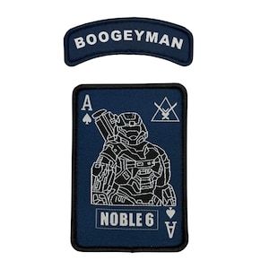 May include: Two embroidered patches. The top patch is a navy blue arc with the word "BOOGEYMAN" in white. The bottom patch is a navy blue Ace of Spades card with a detailed white illustration of a soldier and the words "NOBLE 6".