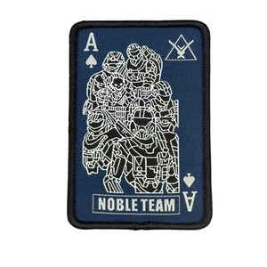 Peut inclure: Un écusson rectangulaire avec un fond bleu marine et une bordure noire. L'écusson présente une illustration blanche d'un groupe de personnages en armure, l'As de Pique, et les mots "NOBLE TEAM".