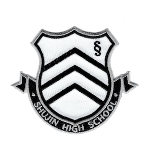 May include: A white and black embroidered patch in the shape of a shield. The shield features two black chevron stripes and a section symbol in the upper right corner. A curved black banner at the bottom displays the text SHUJIN HIGH SCHOOL.