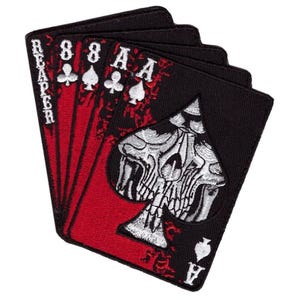 Könnte beinhalten: Ein rechteckiger bestickter Aufnäher mit einem Fächer aus fünf Spielkarten mit schwarzem Rand und rotem Hintergrund. Die Karten zeigen den Text REAPER, die Zahl 8 und den Buchstaben A sowie ein großes weißes Totenkopfmotiv im Pik-Symbol.