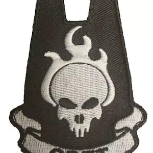 May include: Black and white embroidered patch featuring a skull with flames and the text "ODST" on a banner. The patch has a unique shape with two upward extensions.