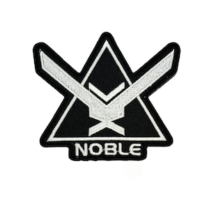 May include: Black and white embroidered patch with the word "NOBLE" at the bottom. The patch features a geometric design with a triangle shape and a stylized bird or wing motif.