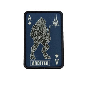 May include: A navy blue patch in the shape of a playing card, with a white illustration of a warrior figure. The text "A" and a spade symbol are in the upper left corner, and "V" and a spade symbol are in the lower right corner. The word "ARBITER" is printed at the bottom.