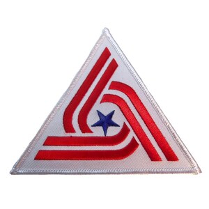 May include: A triangular embroidered patch featuring a white background with a central navy blue five-pointed star. Three sets of double red stripes curve around the star, following the triangular shape of the patch with a white stitched border.