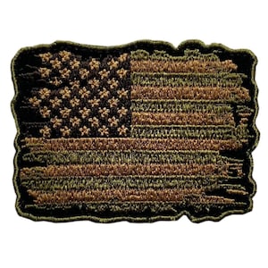 May include: A rectangular embroidered patch featuring a stylized American flag design in shades of olive green, tan, and black. The flag pattern displays a distressed, weathered appearance with embroidered stars and horizontal stripes throughout.