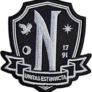 Puede incluir: Un parche bordado en blanco y negro con forma de escudo. El centro presenta una letra N grande, un águila pequeña, una estrella y los números 17 91. Una cinta en la parte inferior muestra el texto UNITAS EST INVICTA en letras mayúsculas blancas.