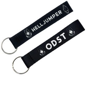 May include: Two black keychains with silver key rings. One keychain reads "HELLJUMPER" in white text, and the other reads "ODST" in white text. Both keychains feature a white skull logo.