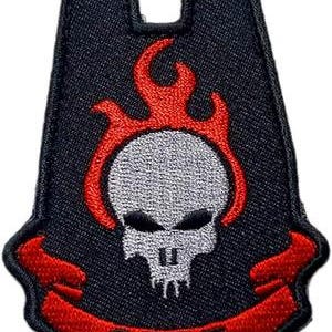May include: Black patch with a red and white skull design, surrounded by red flames. The patch has the letters "ODST" in red on a red banner at the bottom. The patch has a unique shape with a U-shaped top.