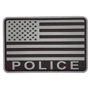 Puede incluir: Un parche rectangular con un diseño estilizado de la bandera estadounidense en tonos gris oscuro y gris claro. La esquina superior izquierda muestra un campo de estrellas, mientras que la parte inferior contiene la palabra POLICE en mayúsculas.