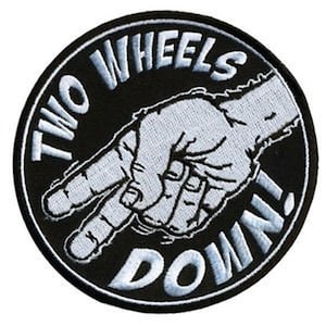 May include: A circular embroidered patch with a black background and a white border. The design features a light grey hand making a downward pointing gesture. The text "TWO WHEELS" is arched at the top and "DOWN!" is at the bottom in white.