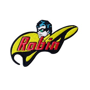 May include: An embroidered patch featuring the word Robin in red letters against a yellow background. Above the text is a stylised illustration of a character with black hair and a green mask. The entire design is outlined in thick black thread.