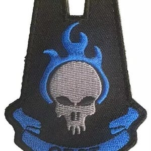 May include: Black embroidered patch featuring a gray skull with blue flames and accents. The patch has the letters "ODST" embroidered in blue on a curved banner. The patch is shaped like a stylized shield.