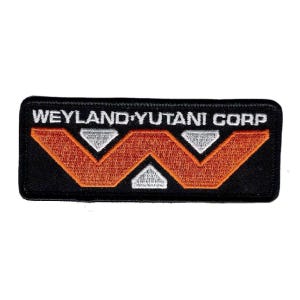 May include: A rectangular embroidered patch with a black background. The text WEYLAND-YUTANI CORP is stitched in white across the top. Below the text is a large orange W-shaped graphic with three silver-grey triangular accents integrated within.