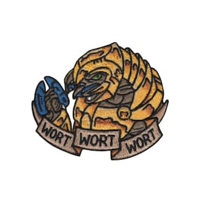 May include: Embroidered patch featuring a stylized creature with yellow, brown, and blue accents. The creature has a stern expression and is holding a blue object. The text "WORT WORT WORT" is displayed on a banner.