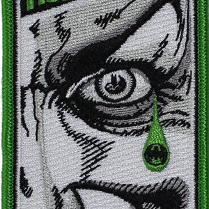 May include: A rectangular embroidered patch featuring a black, white, and green graphic design. The image depicts a close-up of a human eye with a green teardrop containing a black symbol, surrounded by the repeated text HAHAHA in green.