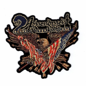 May include: An embroidered patch featuring a bald eagle with spread wings holding an American flag and a rifle. Behind the eagle are several arrows. The text 2nd Amendment 1789 is stitched in gold thread at the top against a dark blue background.