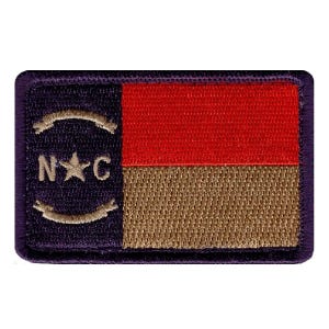 May include: A rectangular embroidered patch featuring a dark blue vertical stripe on the left with the letters N and C flanking a central star, framed by two curved lines. The right side has a horizontal red stripe over a tan stripe.