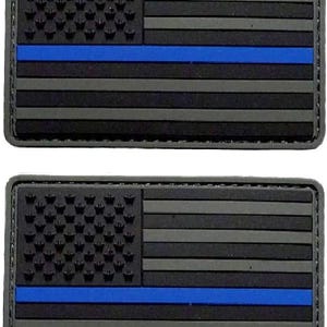 May include: Two rectangular morale patches featuring a stylized American flag design in shades of black and dark gray. A single horizontal blue stripe runs across the center of each patch, contrasting with the monochromatic flag elements.