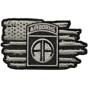 May include: A rectangular embroidered patch featuring a distressed American flag design in shades of black and grey. Centered on the flag is a black square emblem with the word AIRBORNE in white text above a circular logo containing the letters AA.