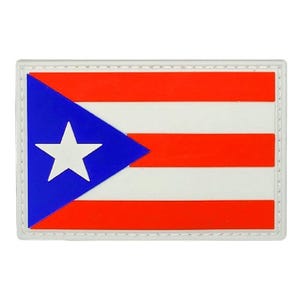 May include: A rectangular PVC patch featuring the flag of Puerto Rico. The design consists of five horizontal stripes in alternating red and white, with a blue triangle on the left side containing a single, centered white five-pointed star.