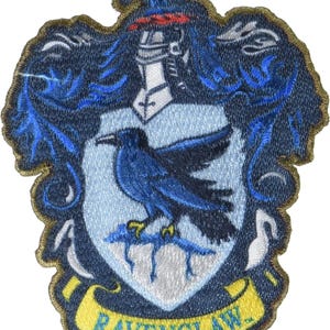 May include: An embroidered fabric patch featuring a crest with a light blue shield, a dark blue raven perched on a branch, a silver knight's helmet, and blue scrollwork. A yellow banner at the bottom displays the text RAVENCLAW in blue letters.