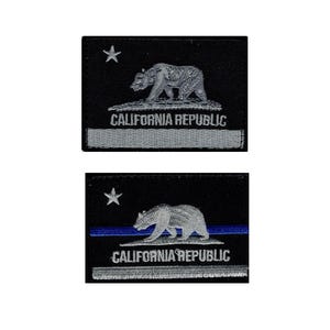 May include: Two rectangular embroidered patches featuring a black background with a white star, a walking bear, and the text CALIFORNIA REPUBLIC. The top patch has a grey stripe, while the bottom patch features a thin blue horizontal line.