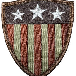 May include: A shield-shaped embroidered patch featuring a dark brown upper section with three white embroidered stars. The lower section displays alternating vertical stripes in copper-brown and light sage green, all bordered by a dark brown stitched edge.