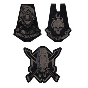 May include: Three embroidered patches in black and grey. The top left patch features a helmeted figure, mountains, and the text REMEMBER REACH. The top right patch shows a flaming skull and the text ODST. The bottom patch depicts a skull with crossed swords.